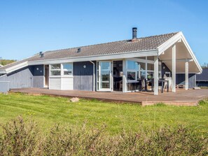 Ein modernes Haus mit einer überdachten Terrasse, großen Fenstern und einem Rasen.