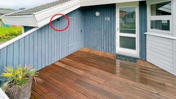 Una propiedad residencial con una terraza de madera, una pared exterior azul y una puerta blanca.