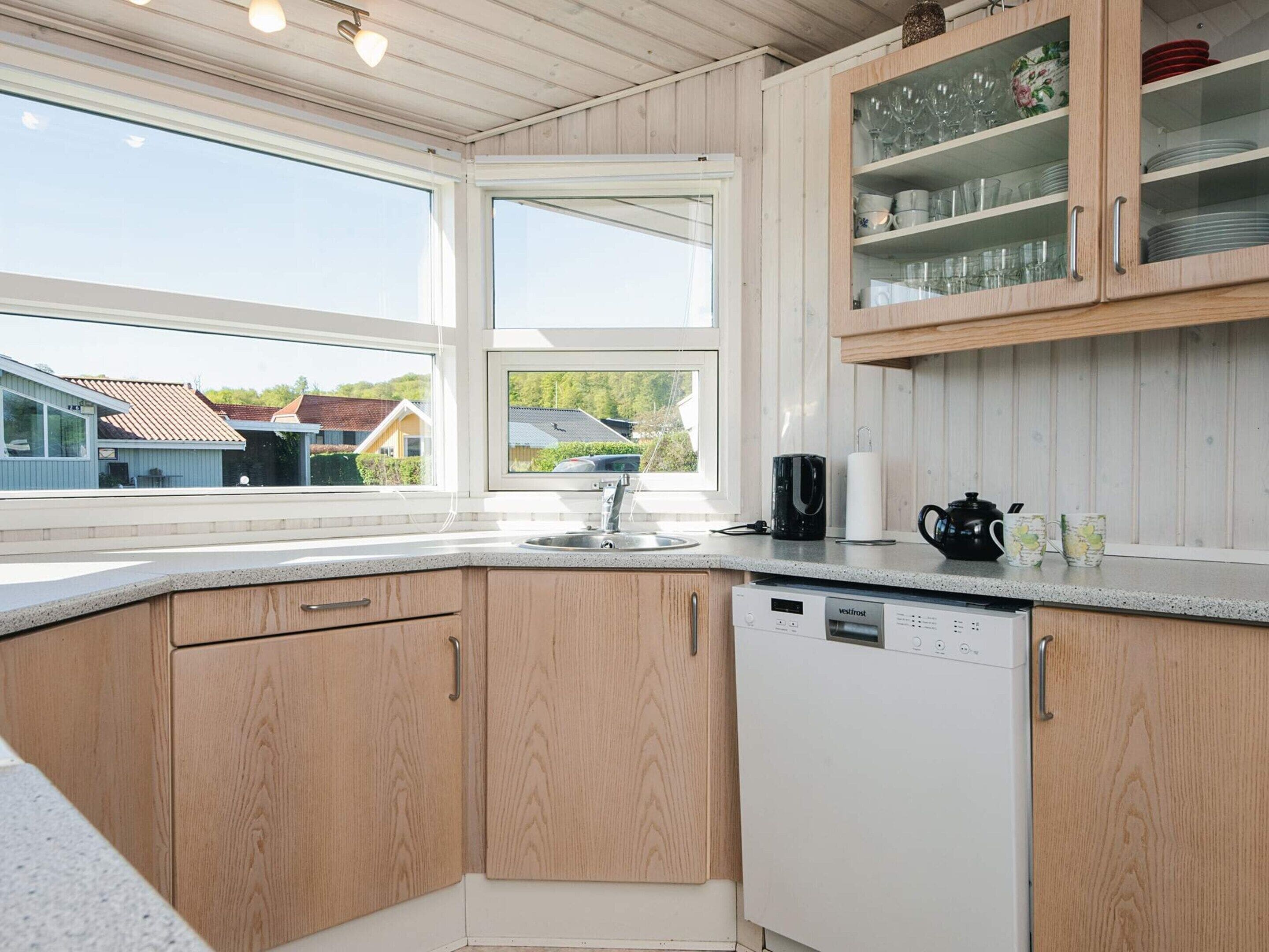 Een keuken met houten kastjes, een vaatwasser en een raam met uitzicht op huizen.