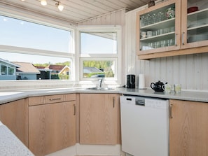 Uma cozinha com armários de madeira, uma máquina de lavar louça e uma janela com vista para casas.