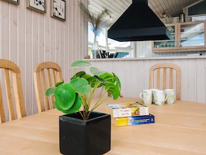 A wooden dining table with a black square planter containing green plants, a stack of books, and two white mugs with a floral pattern. - 4 Star Holiday Home in Sjolund (Sjølund)