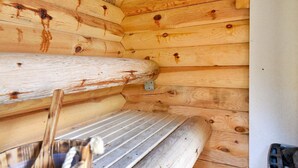 L’intérieur d’une cabane en rondins, avec un banc et un support métallique fixé au mur.