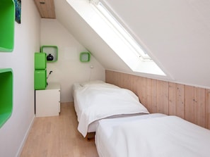 Una piccola camera con un letto singolo, soffitto spiovente e finestra a lucernario, rivestimenti in legno sulle pareti e un comodino verde con una lampada.