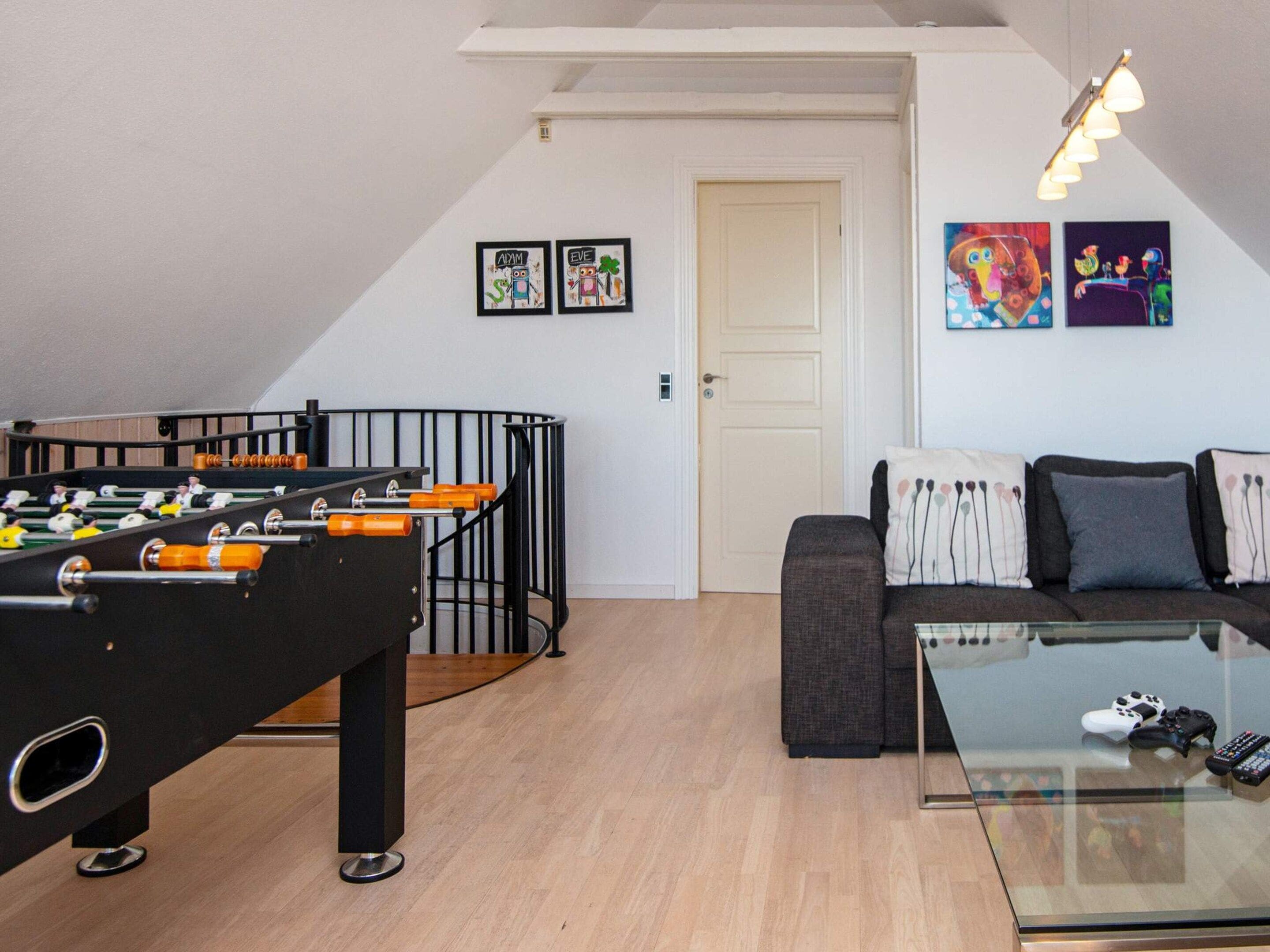 Un soggiorno con tavolo da calcio, divano e tavolino in vetro con telecomandi.