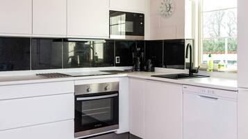 A modern kitchen with white cabinetry, a black microwave, a coffee maker, and a clock on the wall.