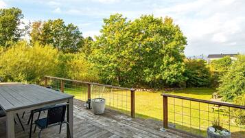A wooden deck with a table and chairs, surrounded by a metal fence and lush greenery.