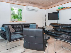 A modern living room with two black leather sofas, a black leather chair, and a flat-screen TV mounted on the wall.