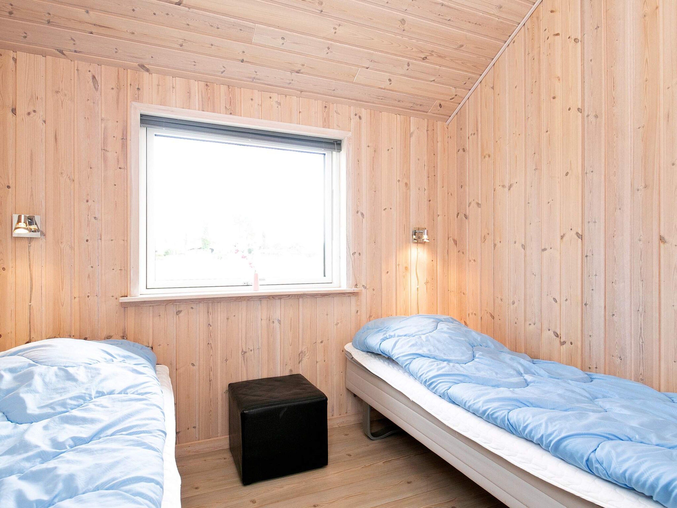 A room with two beds, a window, and a small black ottoman.