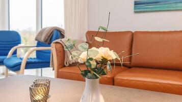 A living room with a white vase containing white flowers and green leaves on a table, a blue chair, and an orange sofa.