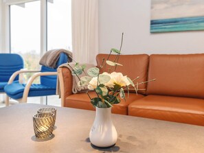 A living room with a white vase containing white flowers and green leaves on a table, a blue chair, and an orange sofa. - 4 Star Holiday Home in Millinge (Millinge)