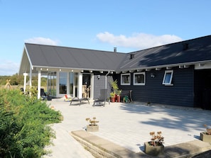 Ein modernes Haus mit überdachter Terrasse, Sitzgelegenheiten im Freien und Topfpflanzen.