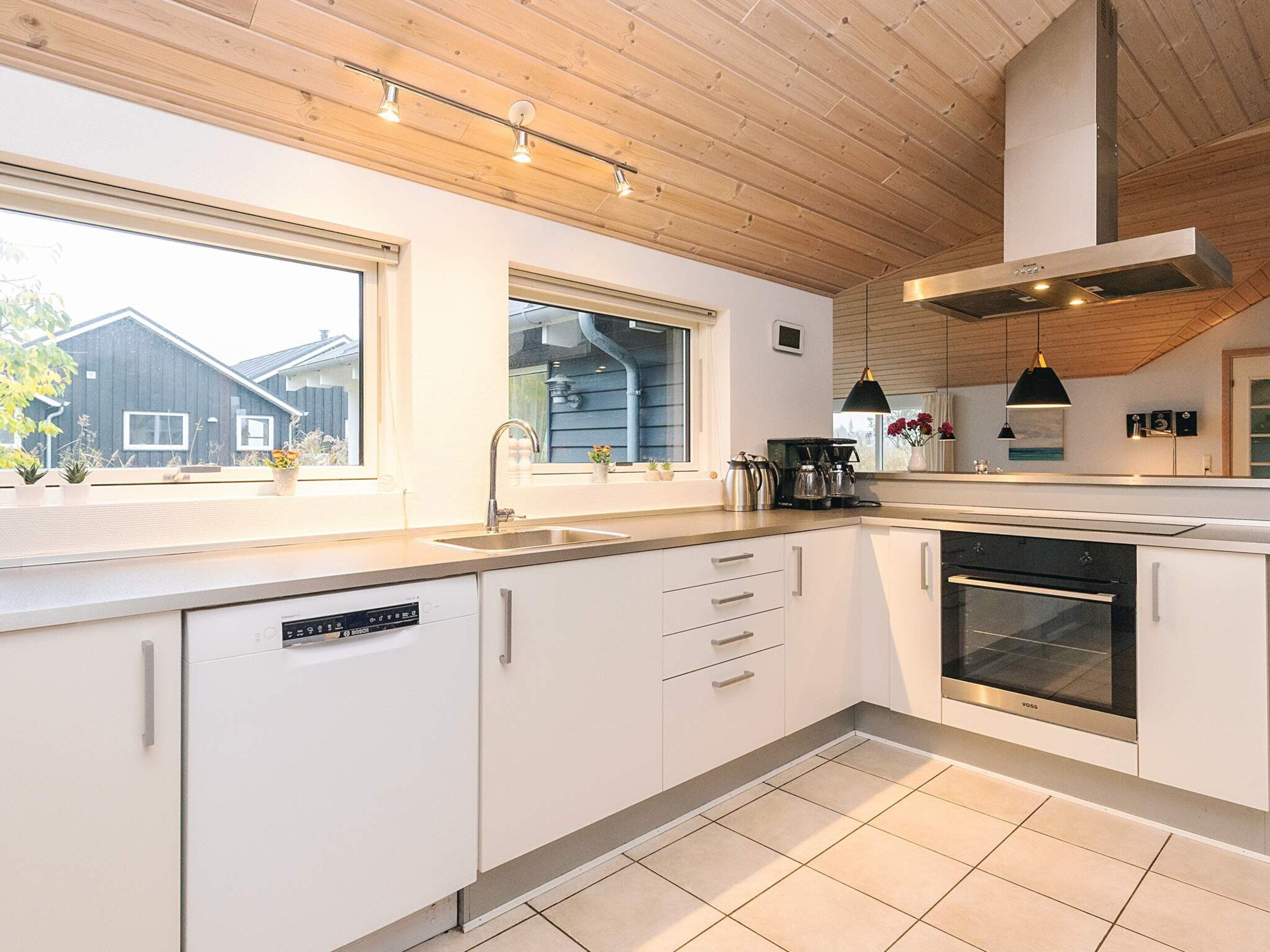 A modern kitchen with white cabinets, a built-in dishwasher, a stove, and a large window providing natural light.