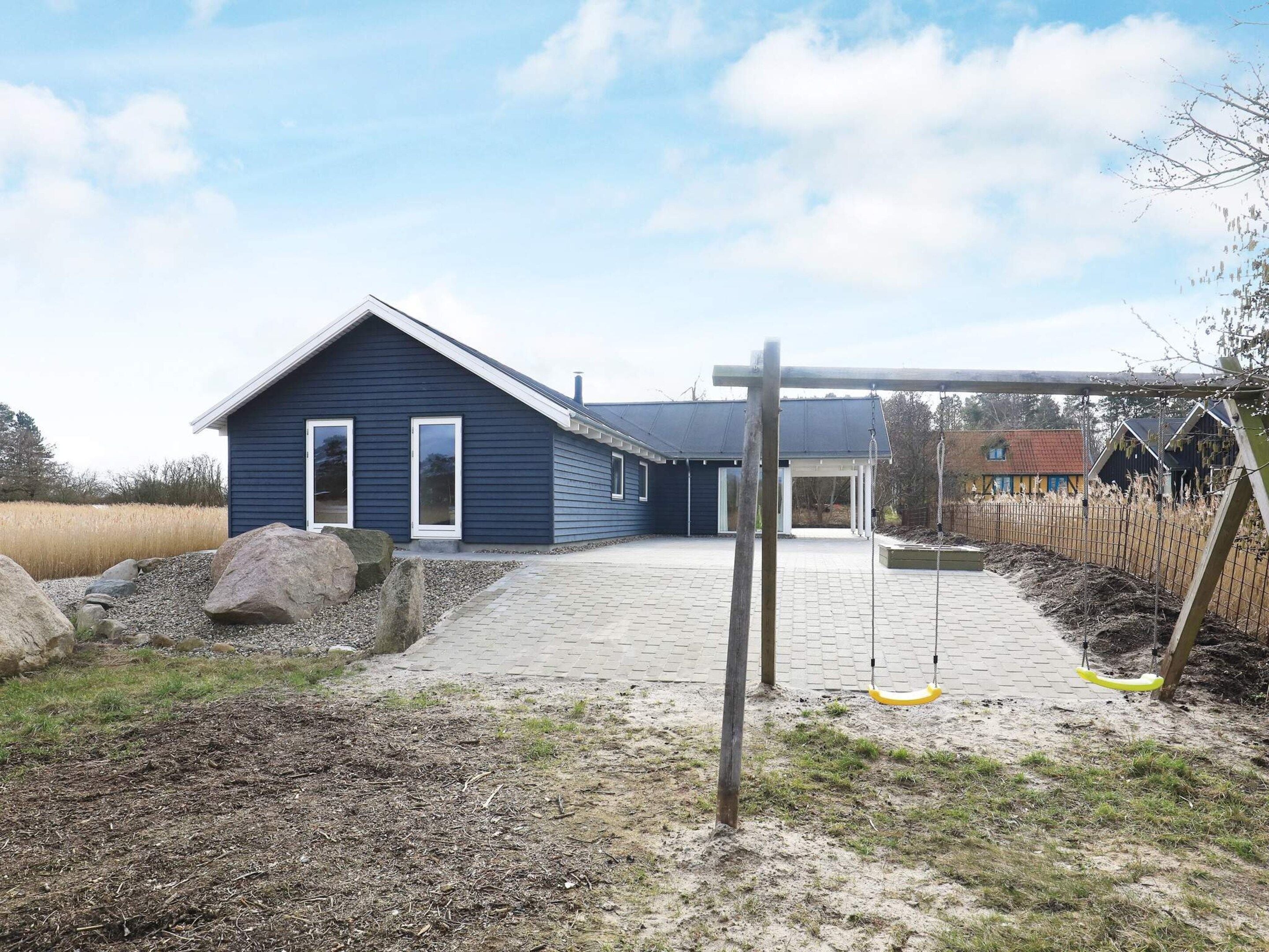 A residential property with a blue house, a paved driveway, and a swing set.