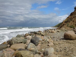 Eine felsige Küstenlinie mit brechenden Wellen am Strand und einer Klippe im Hintergrund.