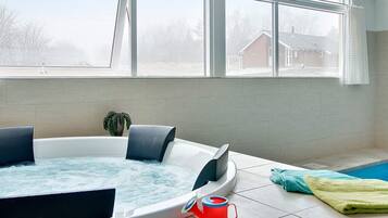 A modern bathroom with a hot tub, a potted plant, and a view of a residential area through large windows.