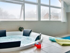 A modern bathroom with a hot tub, a potted plant, and a view of a residential area through large windows. - 5 Star Holiday Home in Tisvildeleje (Tisvildeleje)