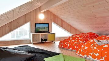 A loft bedroom with a sloped ceiling, a television, a bed with orange and white bedding, and a small wooden cabinet.