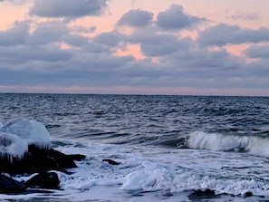 A coastal scene with waves crashing onto rocks and a cloudy sky.