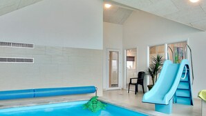 An indoor swimming pool with a slide, a bench, and a chair.