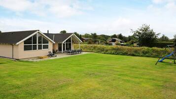 A residential property with a large lawn, a patio with outdoor furniture, and a play area with a slide.