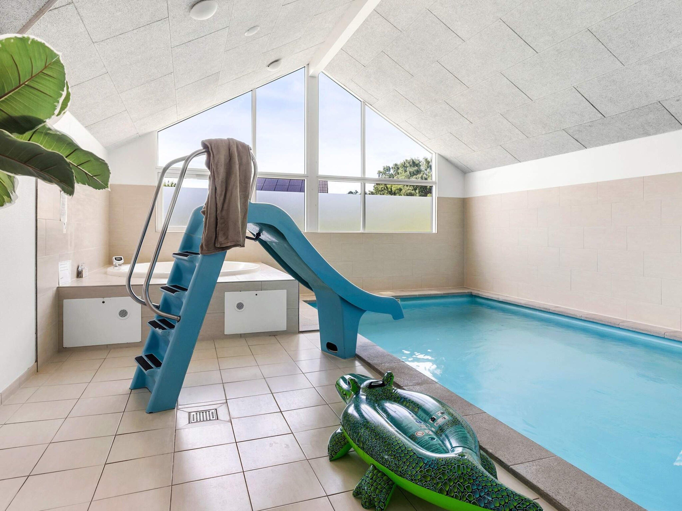 En indendørs swimmingpool med en blå rutsjebane, en grøn oppustelig skildpadde og et håndklædestativ.