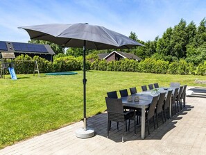 An outdoor patio with a table and chairs, a swing set, and a large umbrella. - 5 Star Holiday Home in Tisvildeleje (Tisvildeleje)