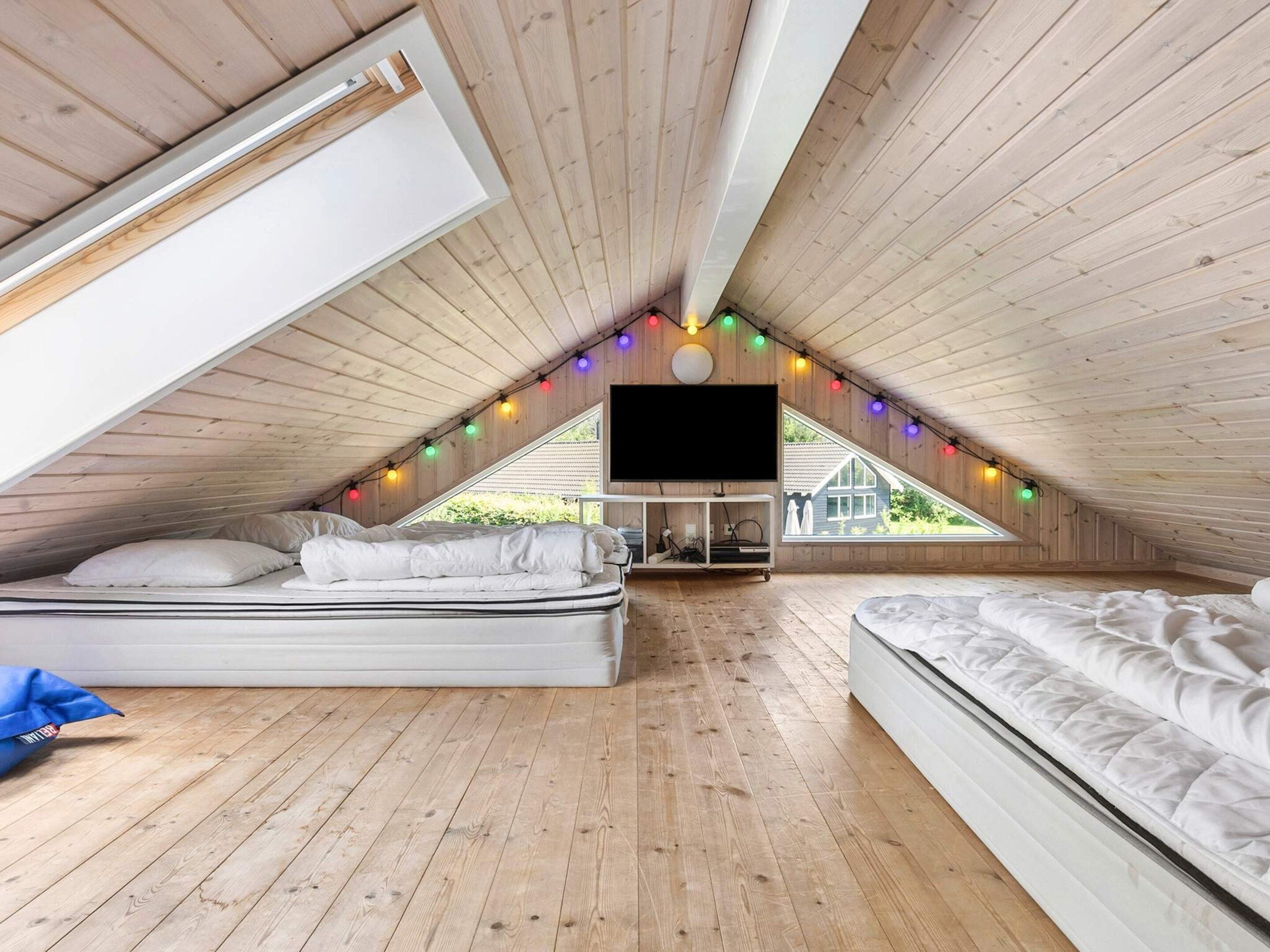 An attic bedroom with wooden floors, two beds, a TV, and a skylight.