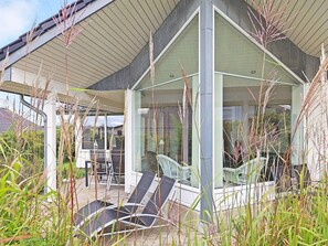 Una casa moderna amb hivernacle de vidre, seients exteriors i herba alta.