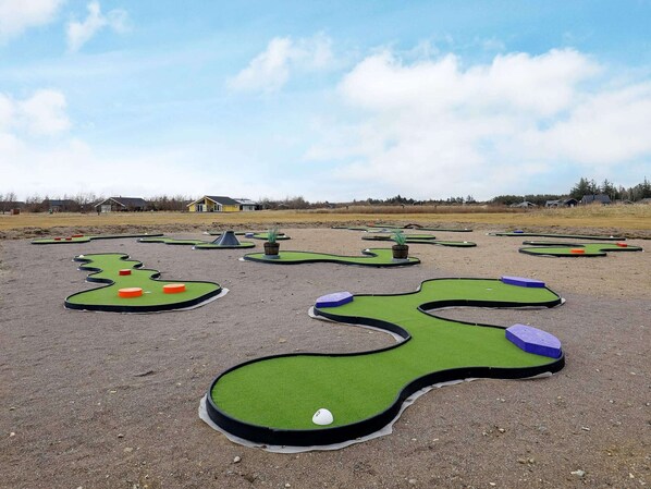 A miniature golf course with multiple holes and a house in the background. - Modern Cottage With Spa - By Traum Ferienwohnungen (Brovst)