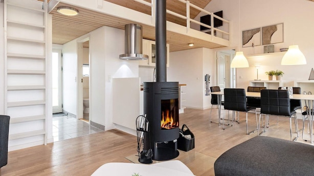 Ett modernt vardagsrum med en vedeldad kamin, en matplats med bord och stolar och ett kök i bakgrunden.