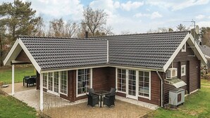 Et hus med skråt tag, store vinduer og en terrasse med udendørs møbler.