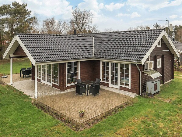 Une maison avec un toit en pente, de grandes fenêtres et un patio aménagé avec du mobilier d’extérieur.