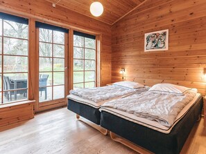 A wooden cabin with two beds, a dining area, and large windows.