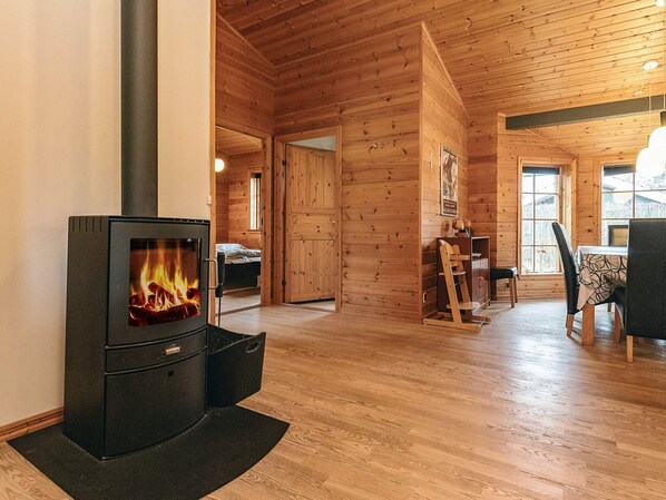 Una cabaña acogedora con estufa de leña, paredes de madera, zona de comedor y una cama al fondo.