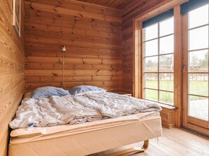 A wooden cabin room with a bed, a window, and a door. - 5 Star Holiday Home in Hadsund (Hadsund)