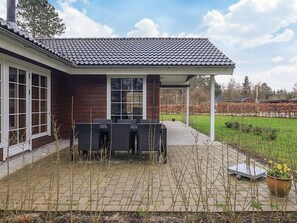 A covered patio with outdoor furniture, a brick pathway, and a garden with trees and shrubs. - 5 Star Holiday Home in Hadsund (Hadsund)