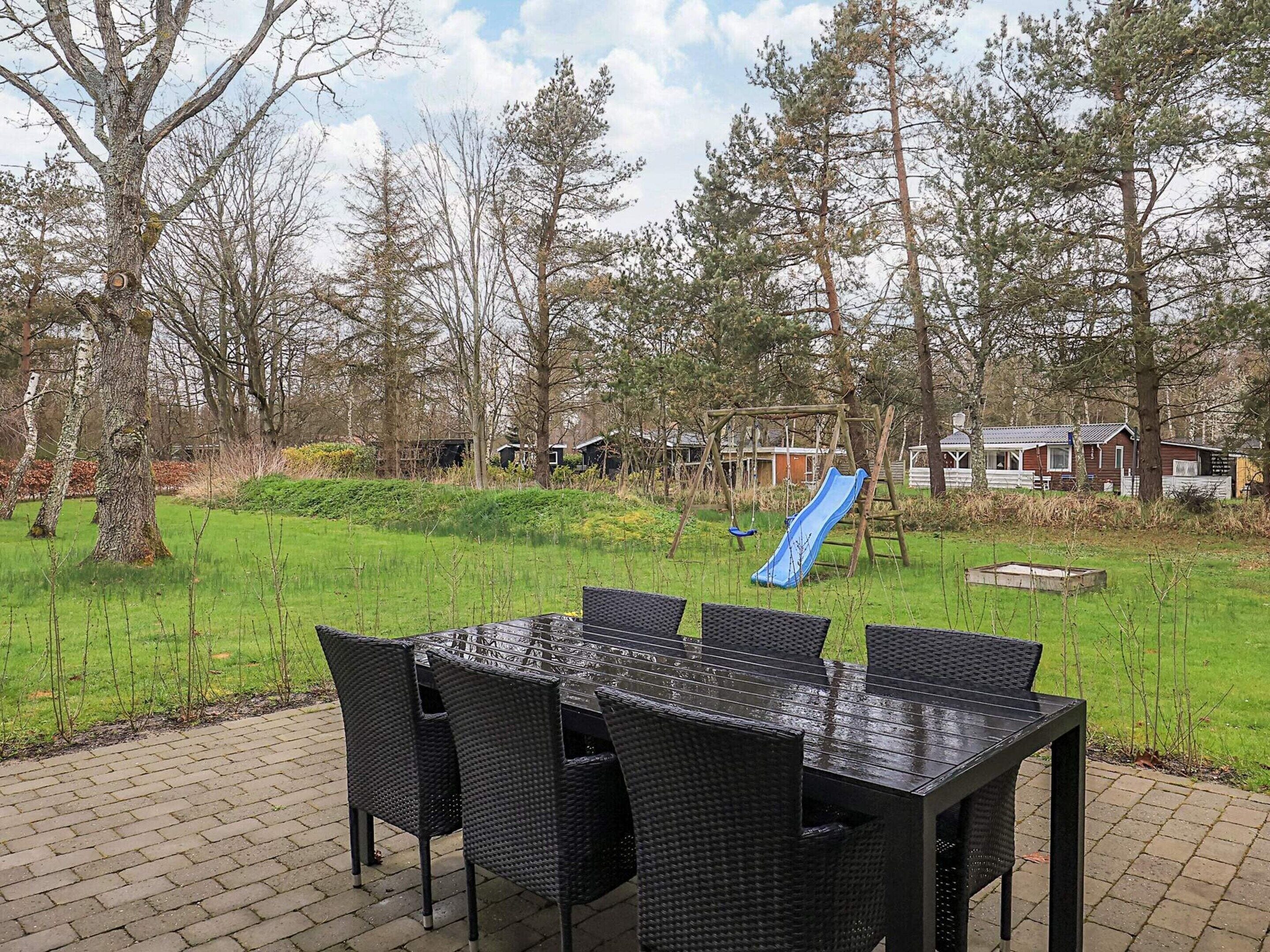 A patio with a table and chairs, a playground with a slide, and trees in the background.