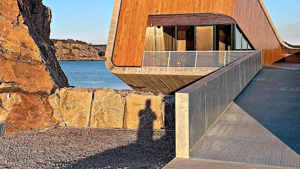 A modern building with a wooden facade and a unique curved design, overlooking a rocky coastline. - 8 Person Holiday Home in Lindesnes-by Traum (Lindesnes)
