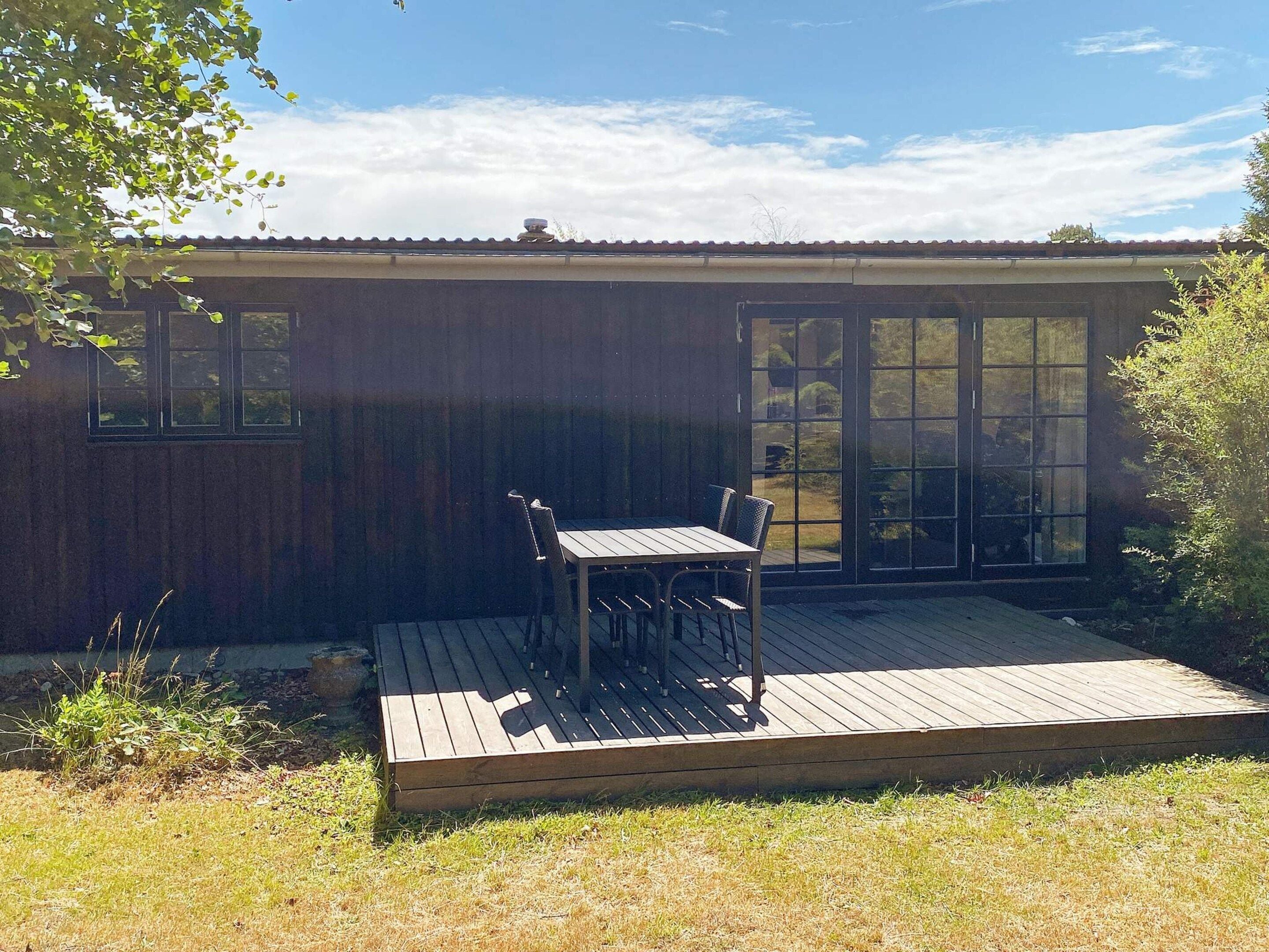 A wooden deck with a table and chairs, a sliding glass door, and a window.