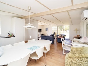 A spacious room with a white dining table, chairs, a sofa, and a TV.