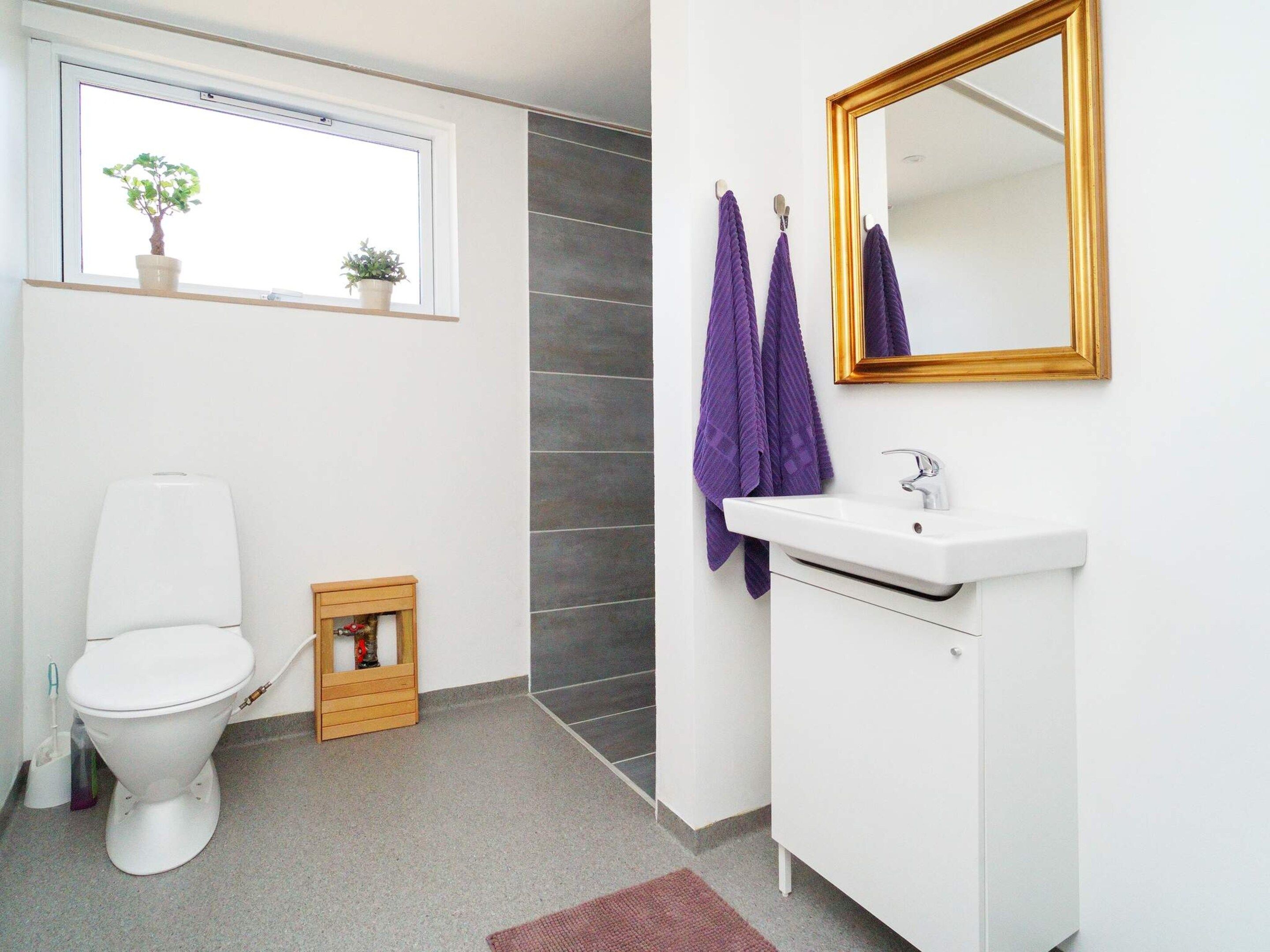 A modern bathroom with a white toilet, a small wooden cabinet, a white sink, and a mirror with a gold frame.