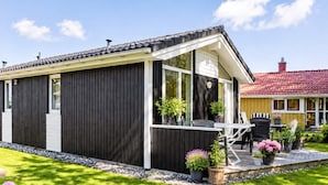 Uma casa moderna com fachada escura, varanda coberta e um pequeno jardim com plantas em vasos.