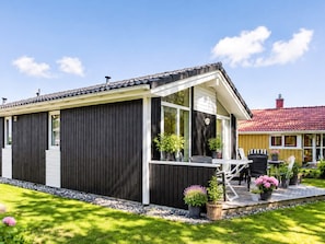 Ein modernes Haus mit dunkler Fassade, einer überdachten Veranda und einem kleinen Gartenbereich mit Topfpflanzen.