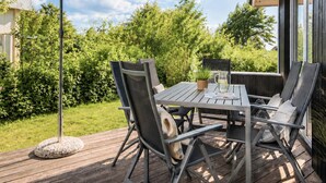 Um pátio externo com mesa e cadeiras, um vaso de plantas e um grande guarda-sol.