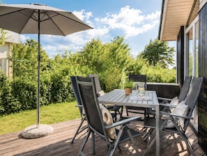Eine Terrass mit Tisch, Stühlen, einer Zimmerpflanze und einem großen Sonnenschirm.
