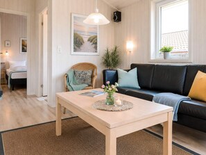 A modern living room with a wooden table, a black leather sofa, and a wicker chair. - Holiday Home in GrÃ¶mmitz (Groemitz)