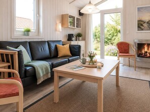 A cozy living room with a black leather sofa, a wooden coffee table, and a fireplace. - Holiday Home in GrÃ¶mmitz (Groemitz)