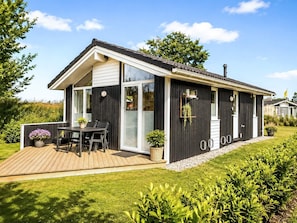 Ein modernes Mobilheim mit Terrasse, großen Fenstern und einem gepflegten Garten.