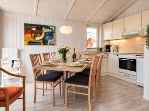 A dining area with a wooden table set for four, surrounded by chairs with black cushions. A painting is visible on the wall above the table. - Holiday Home in GrÃ¶mmitz (Groemitz)