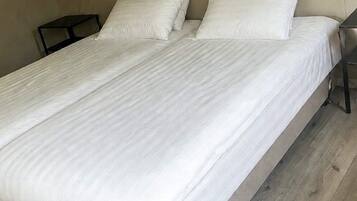 A single bed with white bedding in a room with a wooden floor and a nightstand with a lamp.